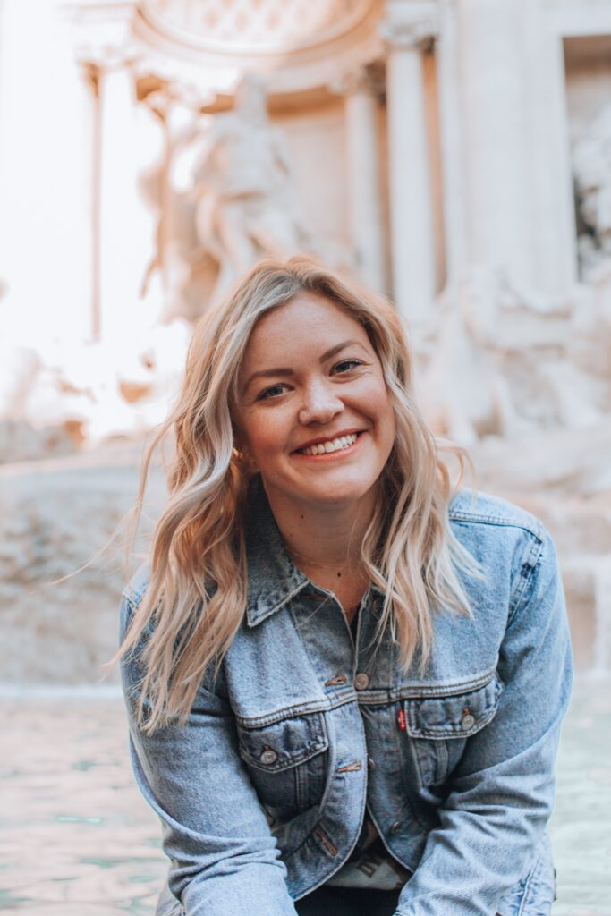 Picture of a woman traveling, smiling in front of the Trevi Fountain