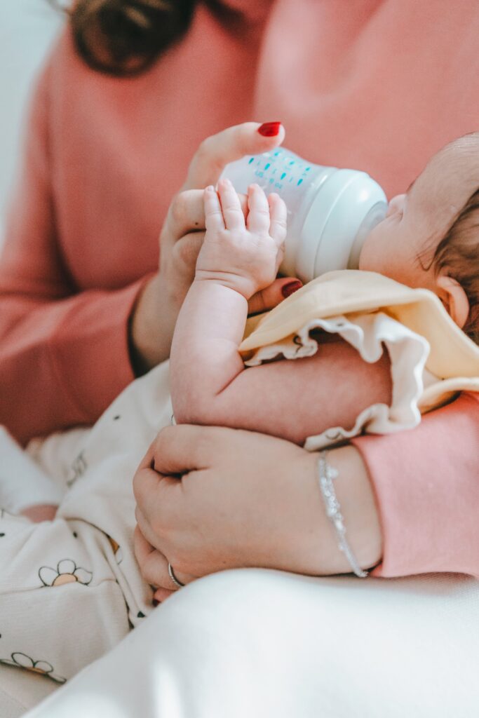 Baby on woman's lap drinking milk from a baby bottle