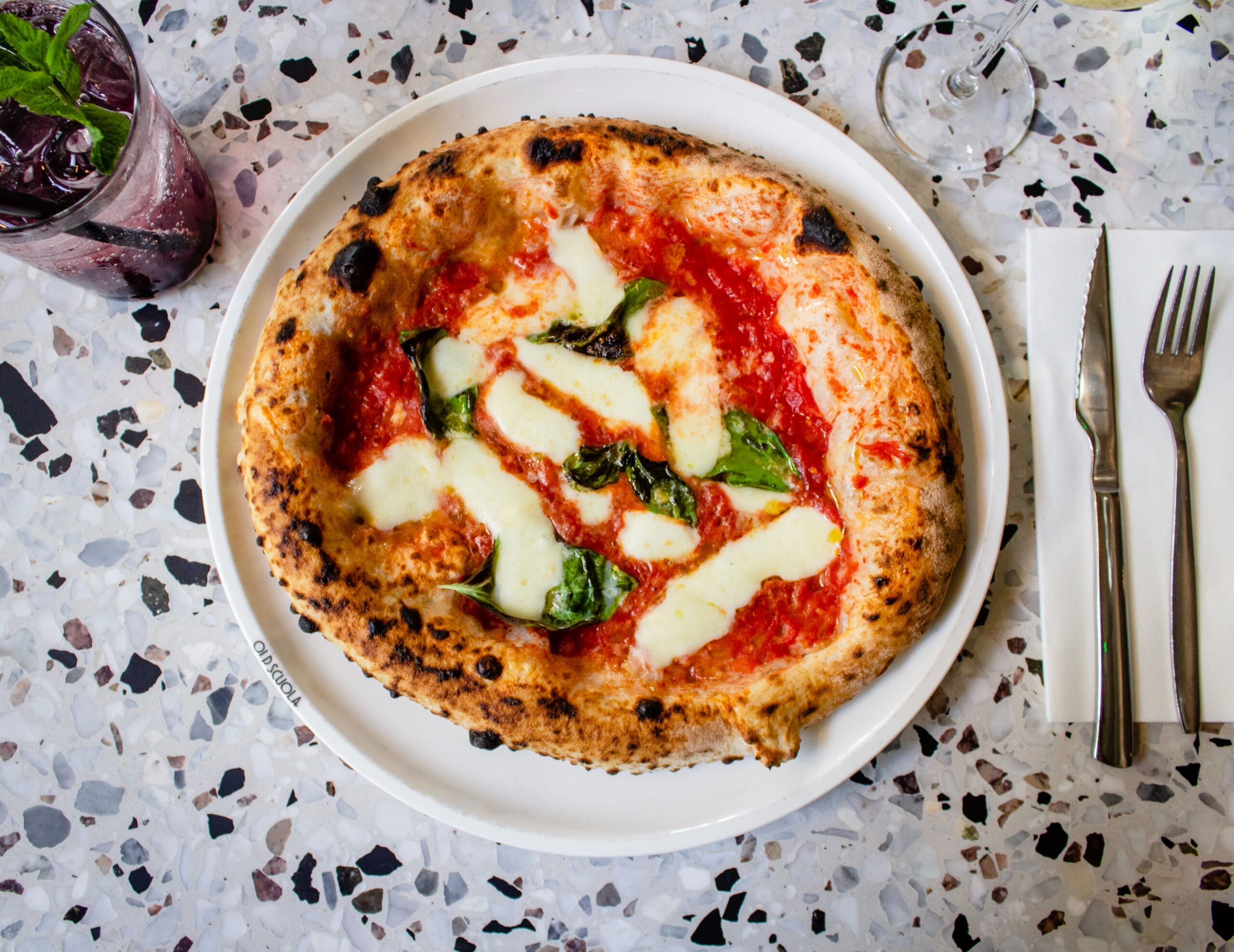 A Neapolitan pizza on a table, with a knife and a fork beside it