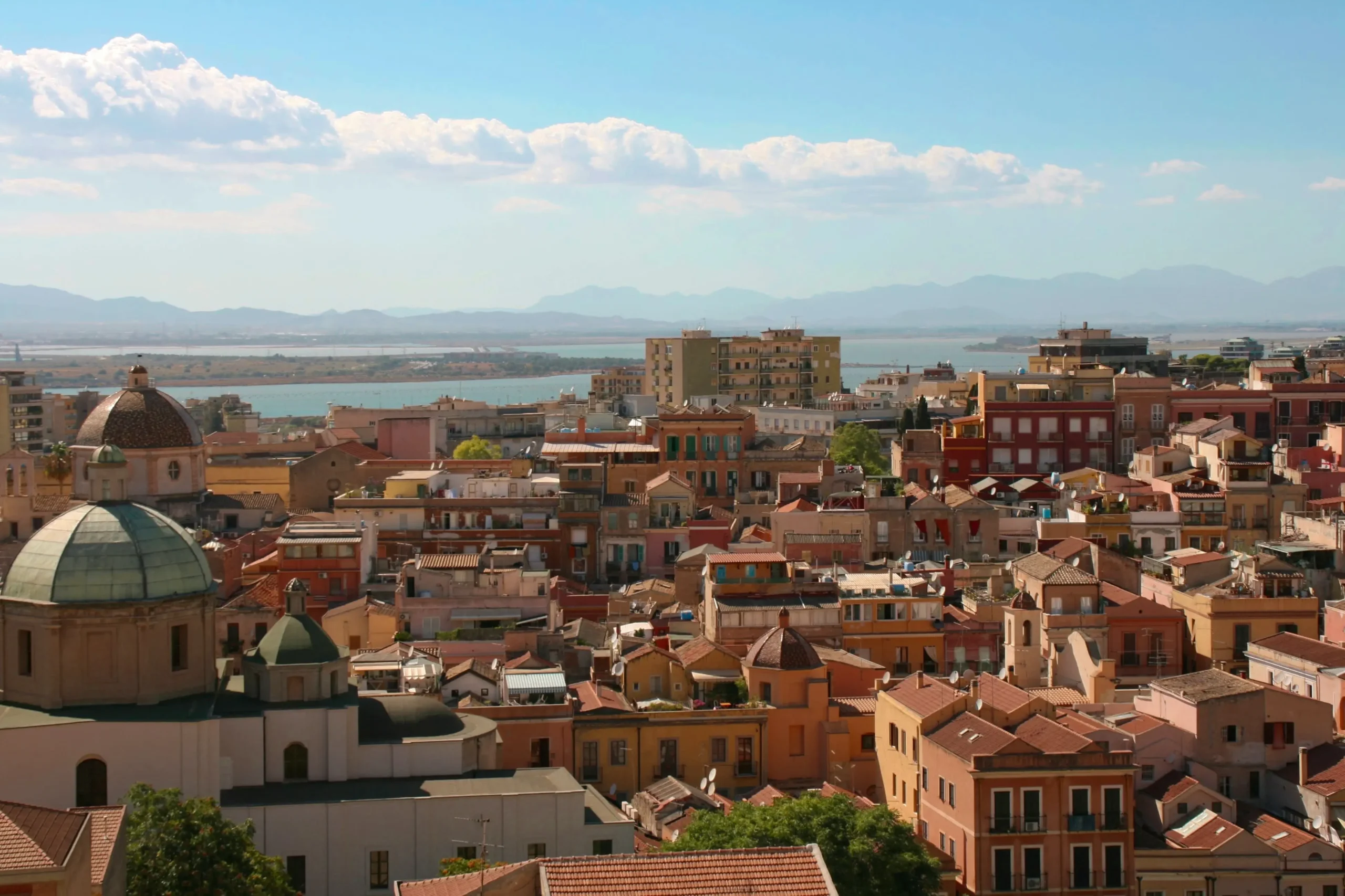 View of the city of Cagliari from above. You can see the rooftops and the sea in the distance.