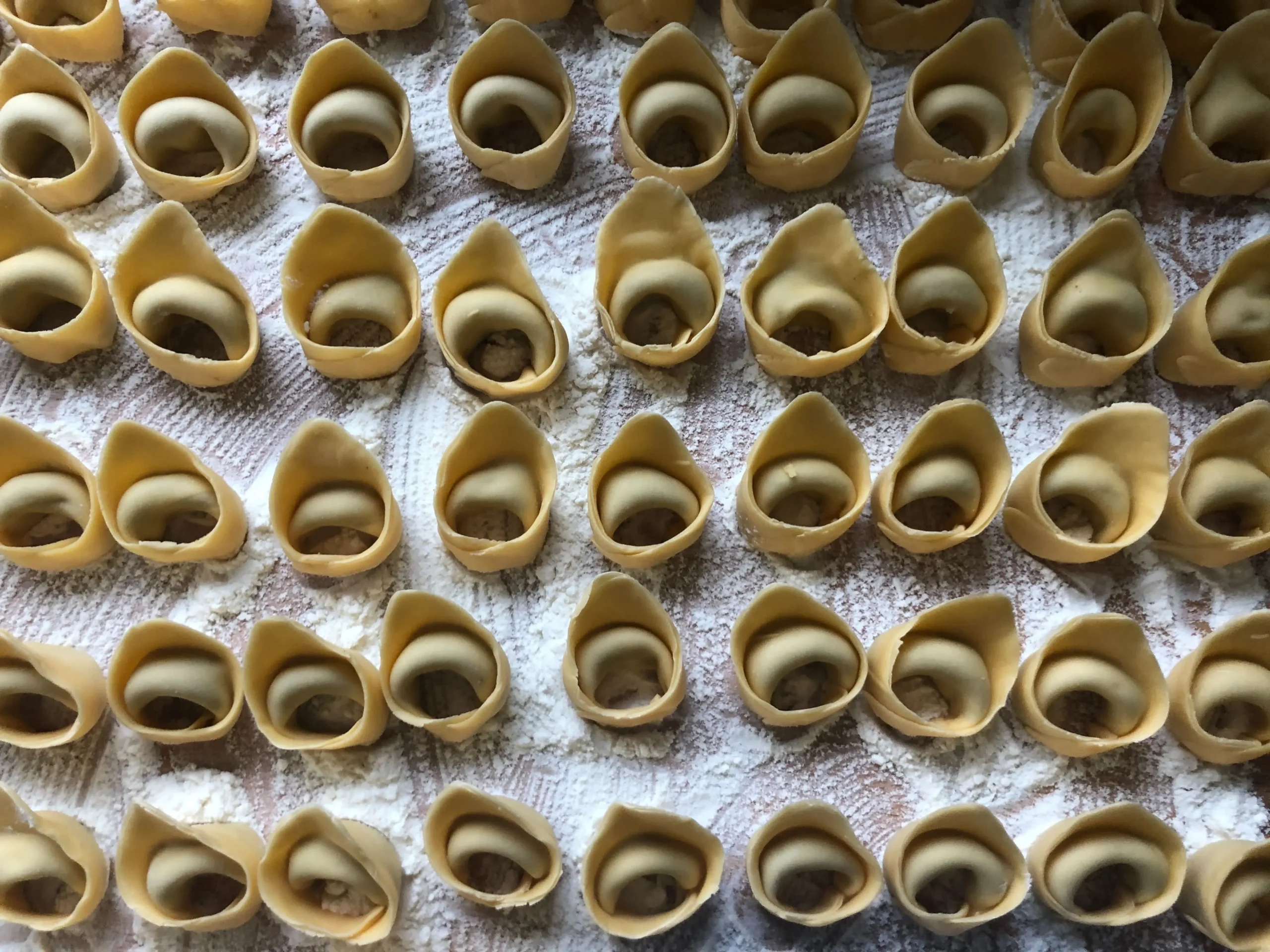 A table covered in flour and a type of fresh, handmade Italian stuffed pasta: tortellini.