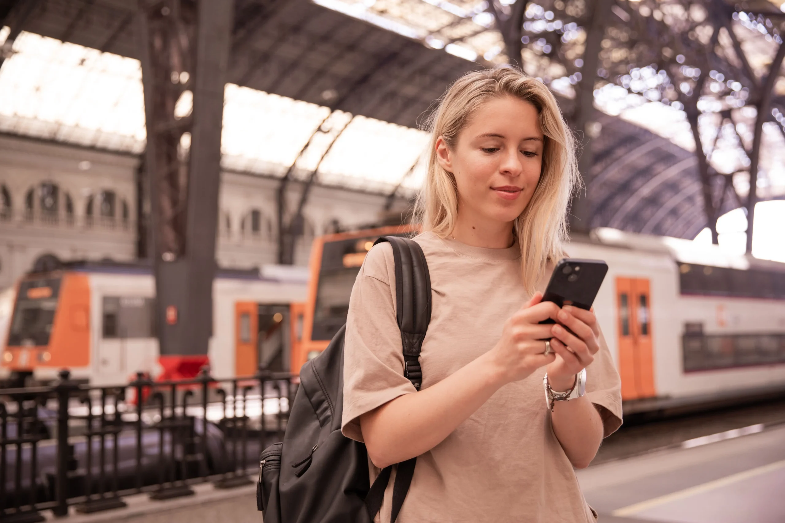 A girl at a train station is searching on her phone for the best train for her.